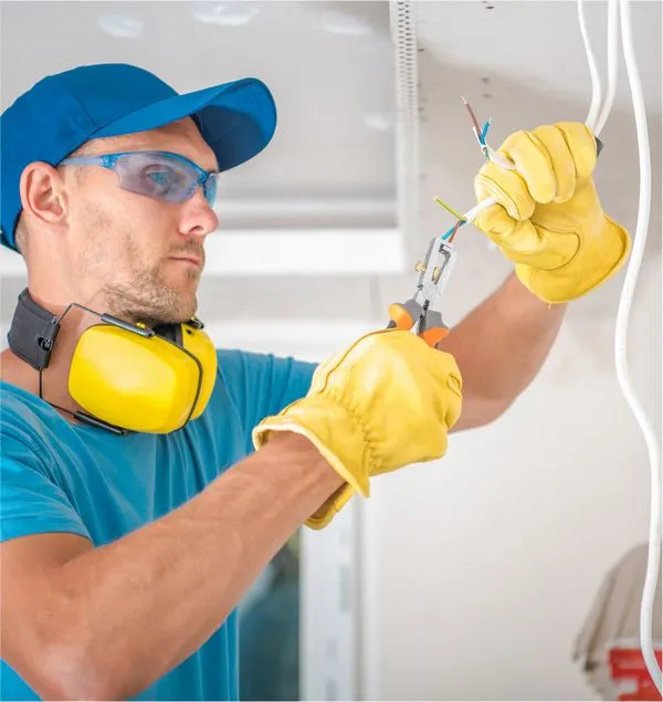 Electrician in safety glasses and gloves terminating wiring at a ceiling rough-in